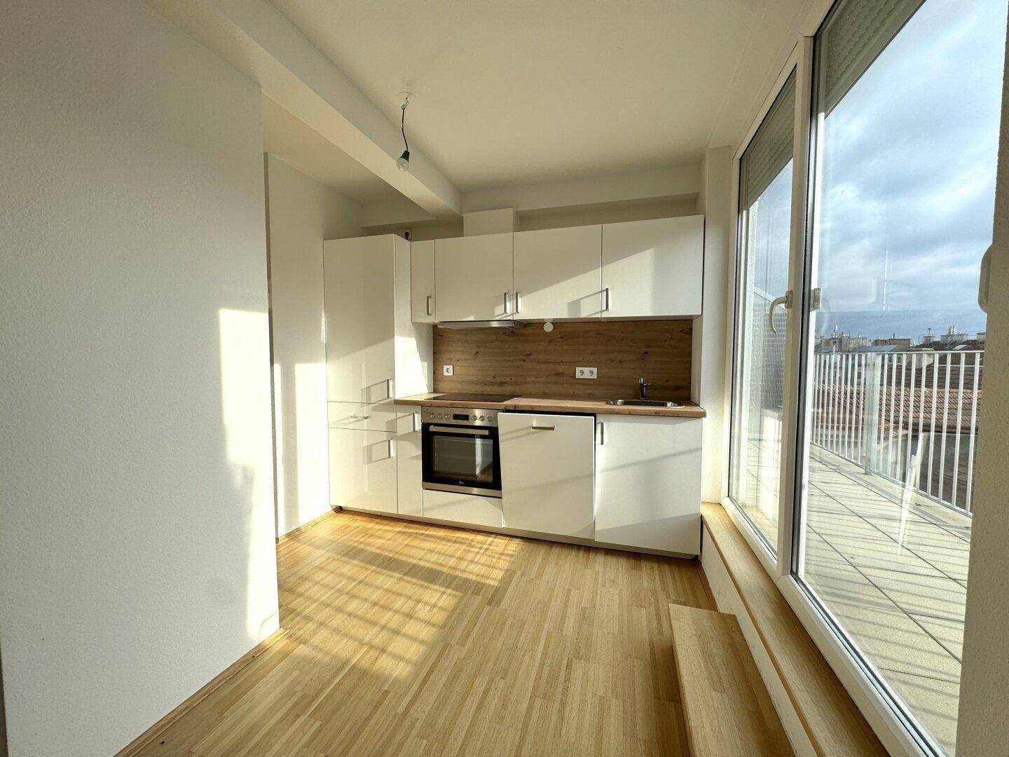Moderne Einbauküche mit weißen Schränken, Holzarbeitsplatte und Zugang zur Terrasse.
