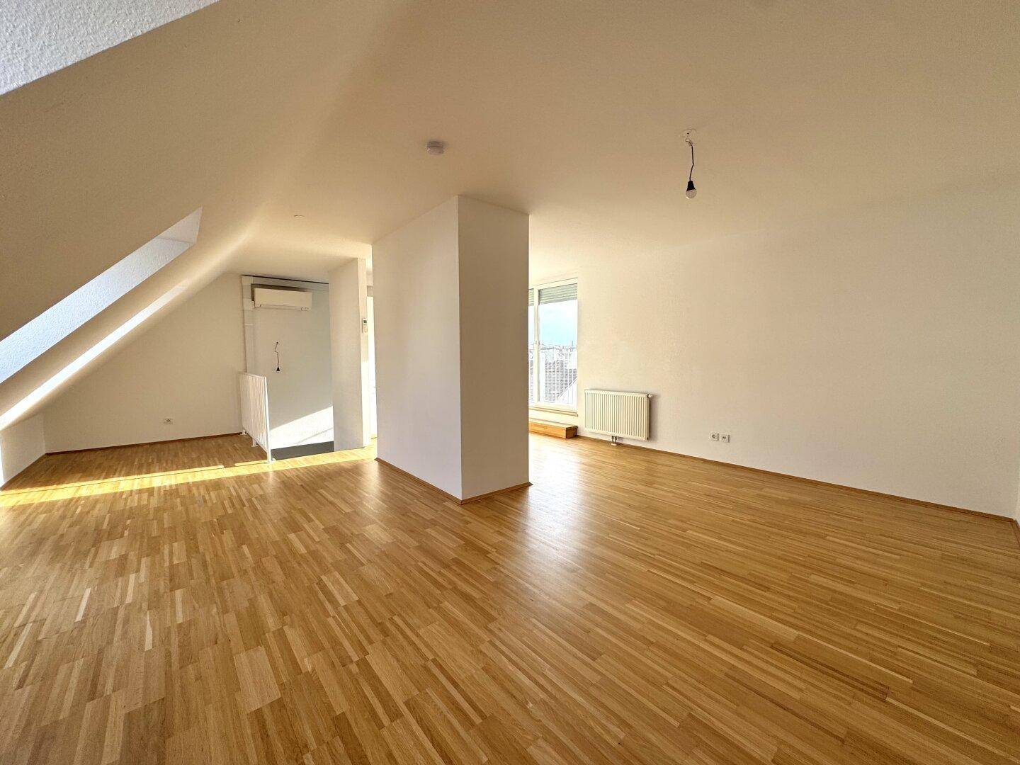 Leerer, heller Wohnbereich mit Holzboden, Dachschrägen und großen Fenstern, in gutem Zustand.