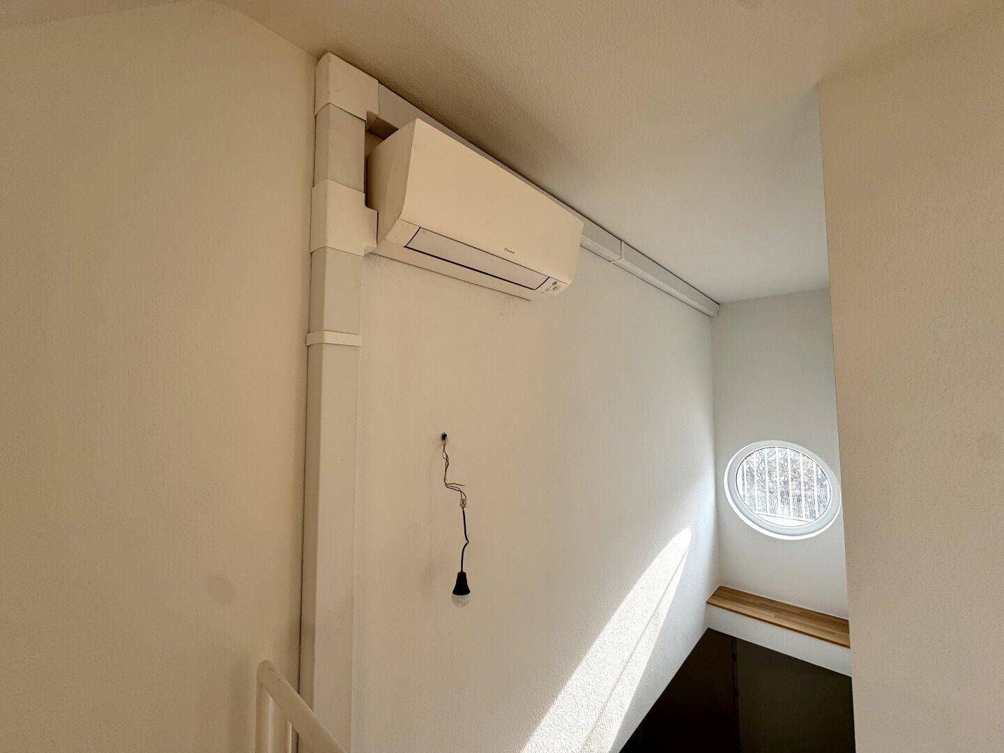 Wand mit installierter Klimaanlage und einem runden Fenster in einem hellen Flur.