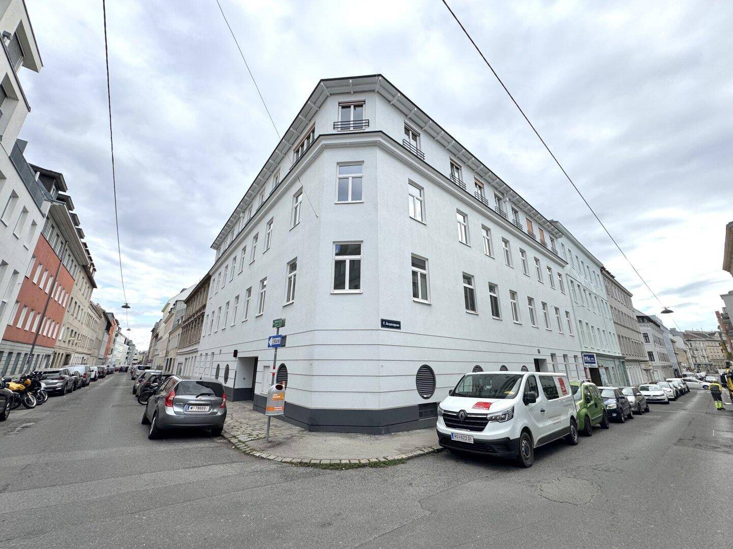 Eckgebäude mit weißer Fassade und vielen Fenstern an einer Stadtstraße.