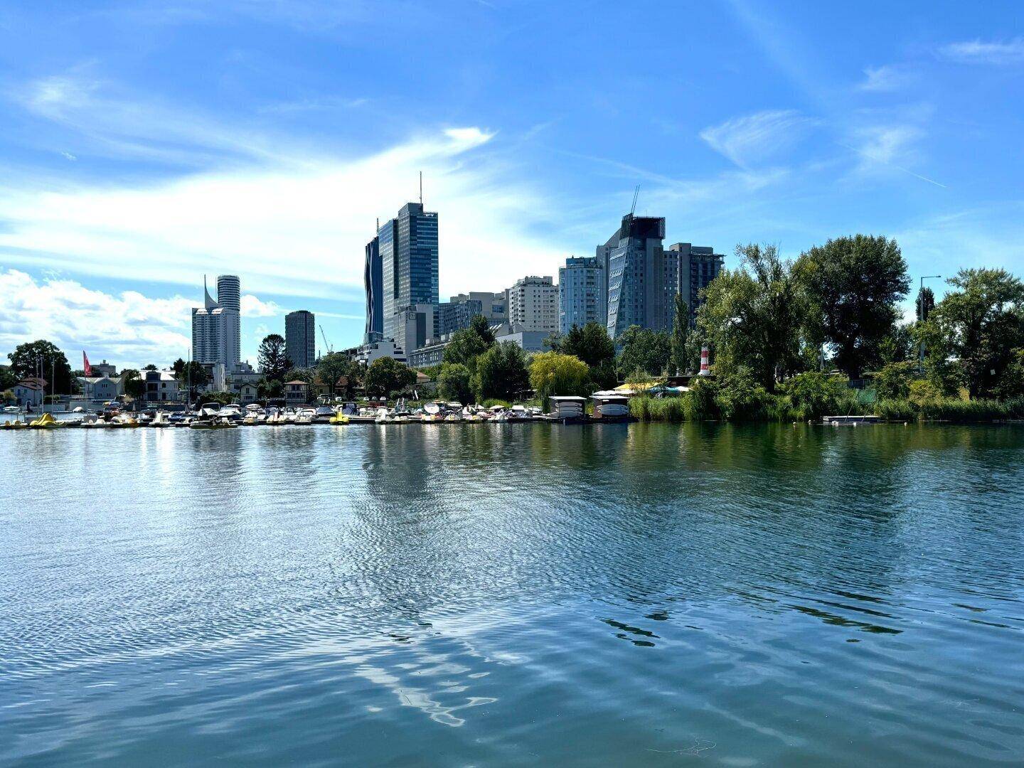 Blick über einen Fluss mit zahlreichen Booten und der modernen Skyline einer Stadt im Hintergrund.