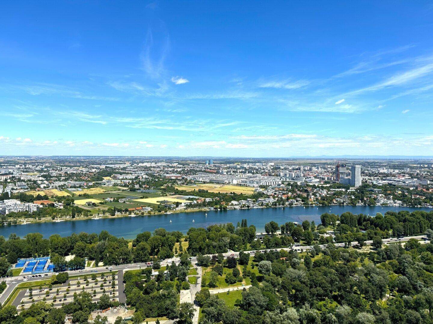Weitläufiger Panoramablick über die Stadt, den Fluss und ausgedehnte Grünflächen unter blauem Himmel.