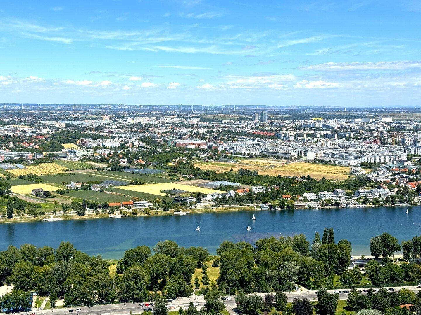 Breiter Überblick über die Stadtlandschaft mit Fluss, Feldern und Wohngebieten unter strahlendem Himmel.