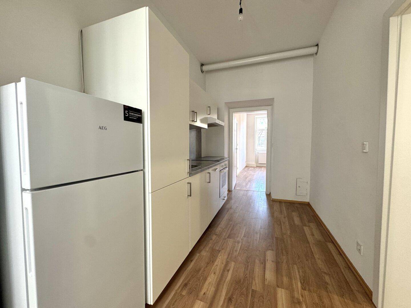 Schmale Küche mit weißen Schränken, Kühlschrank und Holzboden, bereit zur Einrichtung.