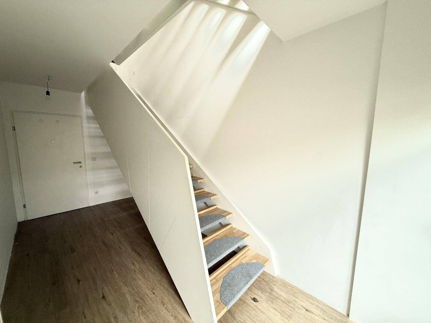 Moderner Treppenaufgang mit Holzstufen und weißer Verkleidung, der die Etagen miteinander verbindet.
