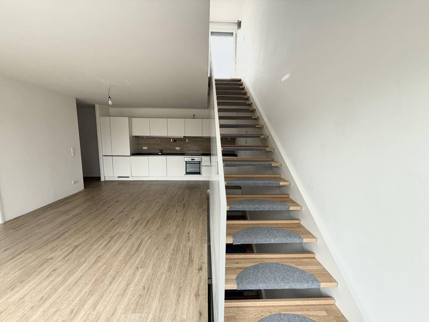 Moderner Wohnbereich mit offener Küche und einer eleganten Holztreppe, die in die nächste Etage führt.