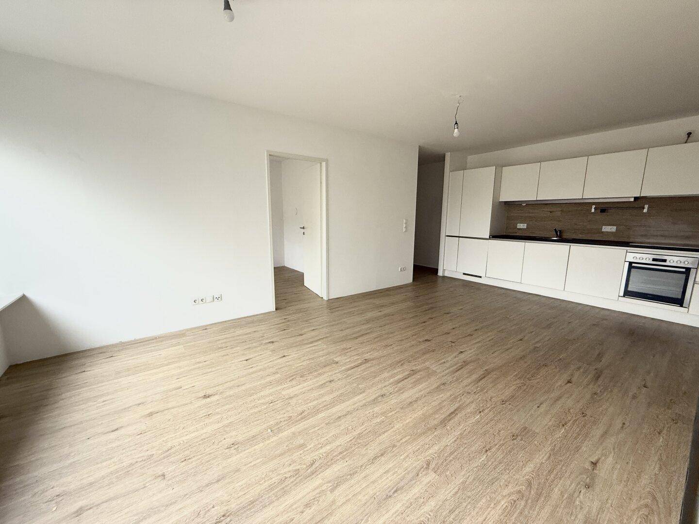 Heller Wohnbereich mit integrierter, moderner Küche und pflegeleichtem Laminatboden, bereit zum Einzug.