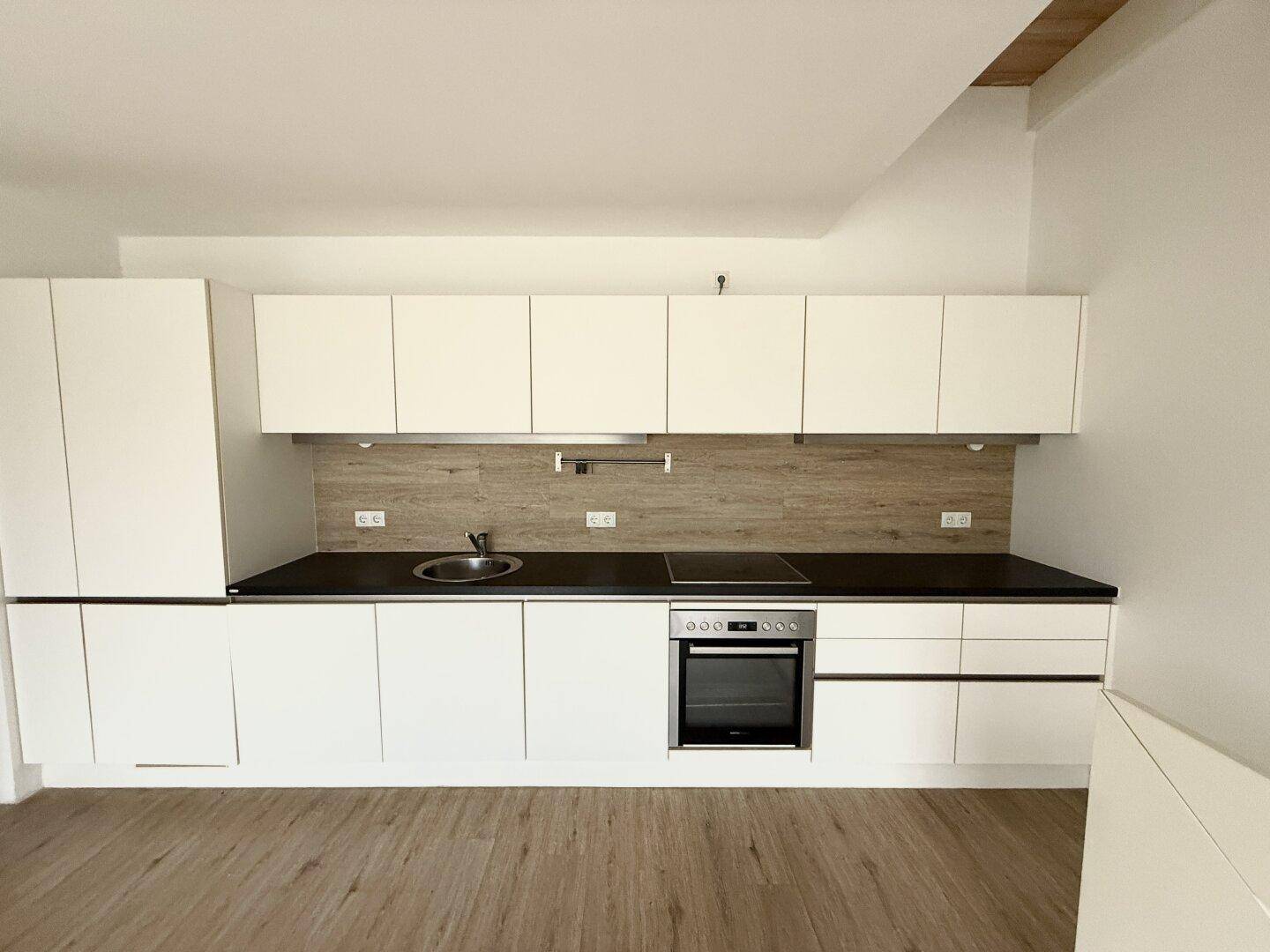 Moderne Einbauküche in Weiß mit dunkler Arbeitsplatte und integrierten Geräten, neuwertig und funktional.
