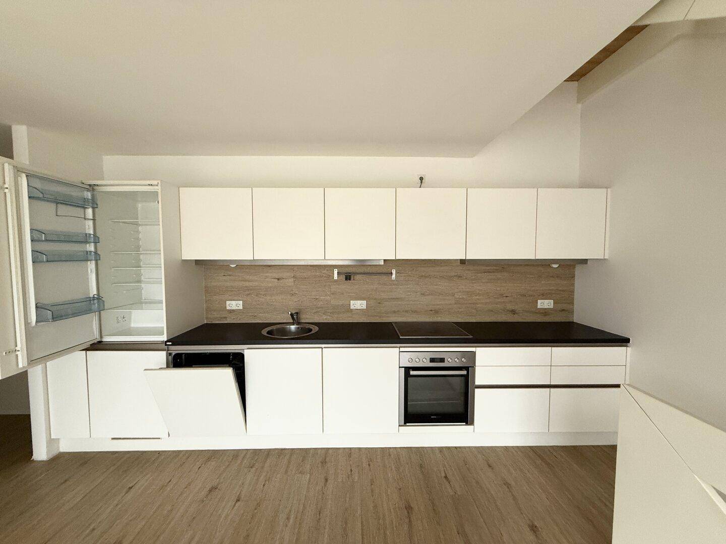 Voll ausgestattete, moderne Küche mit weißen Schränken, dunkler Arbeitsplatte und geöffnetem Kühlschrank.