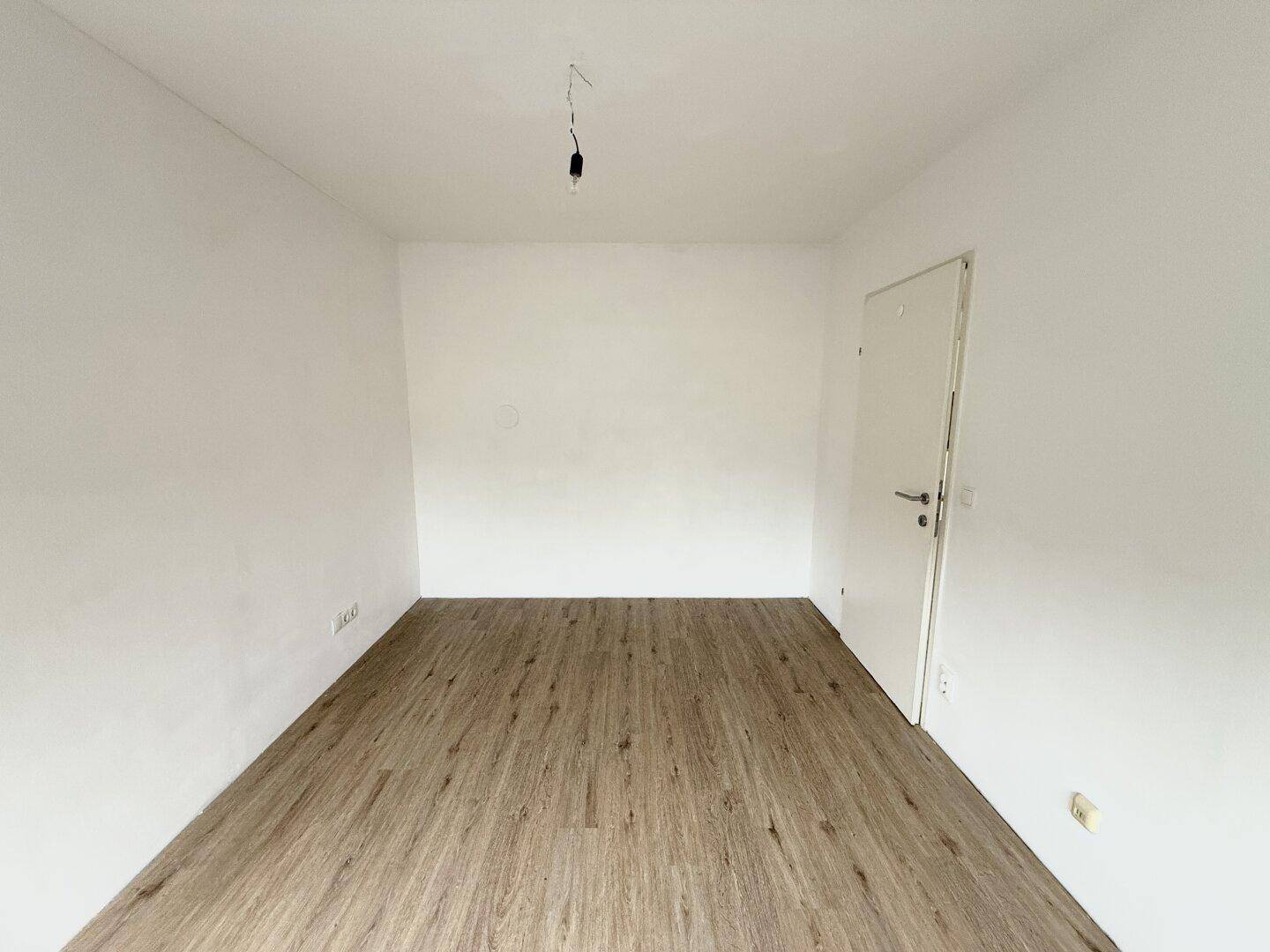 Leeres Zimmer mit Laminatboden und weißer Tür, bietet vielseitige Nutzungsmöglichkeiten für Bewohner.