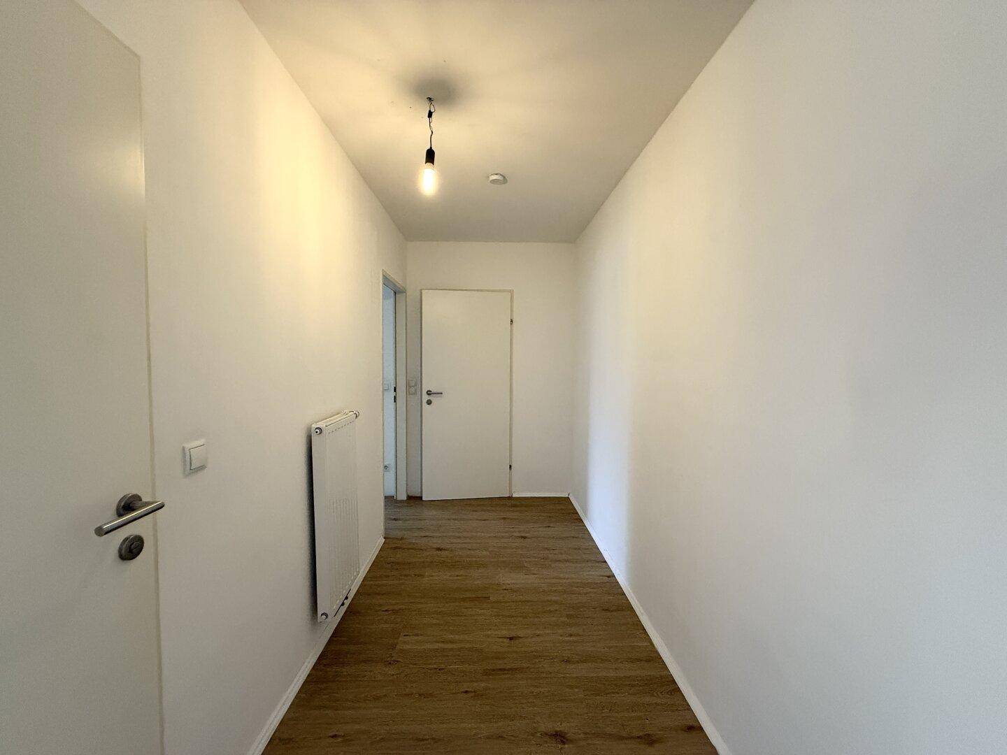 Heller Flur mit Laminatboden und weiß gestrichenen Wänden, der zu weiteren Räumen führt.
