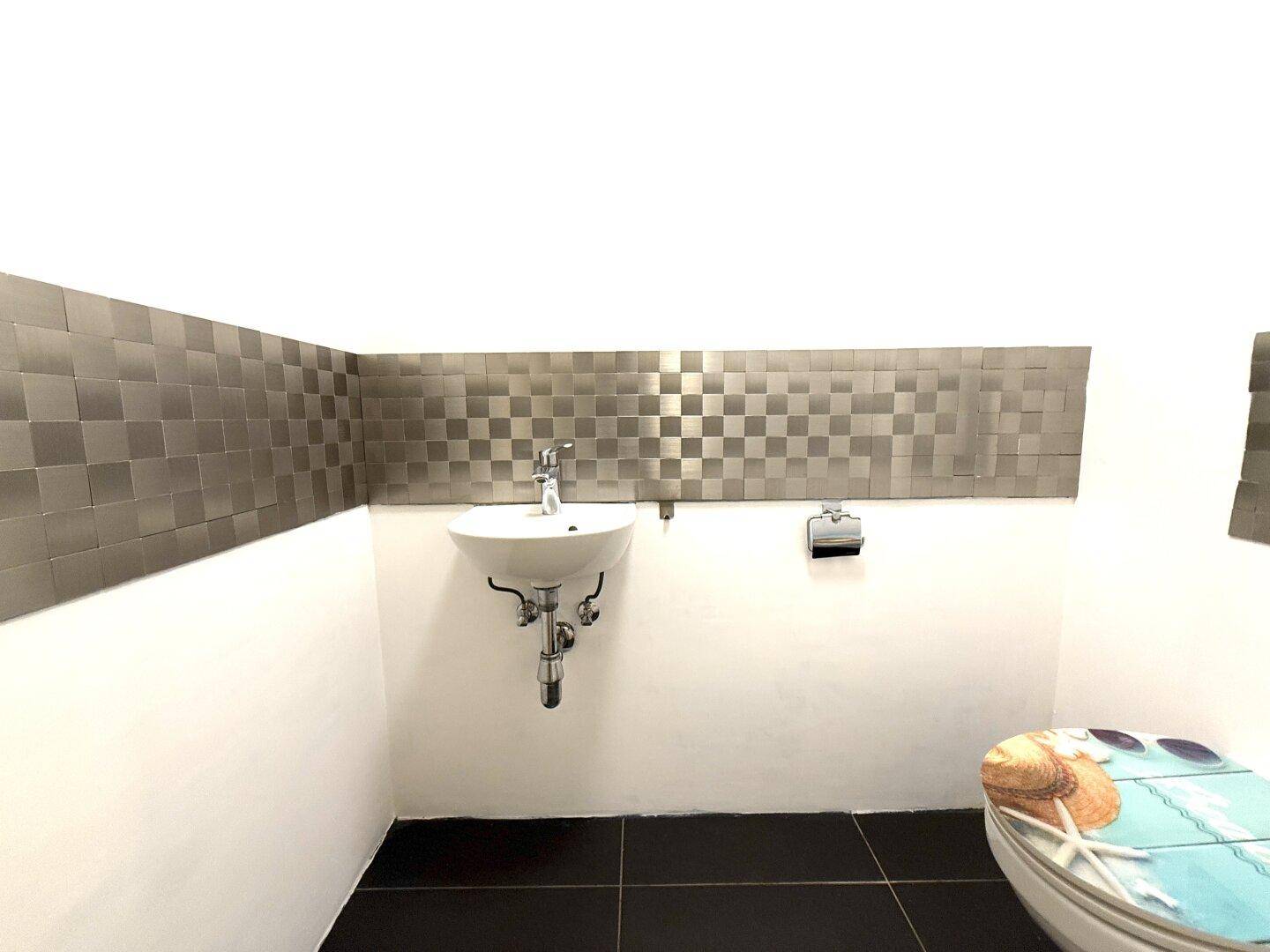 Modernes Gäste-WC mit kleinem Waschbecken, Wandfliesen und dekorativem Toilettensitz.