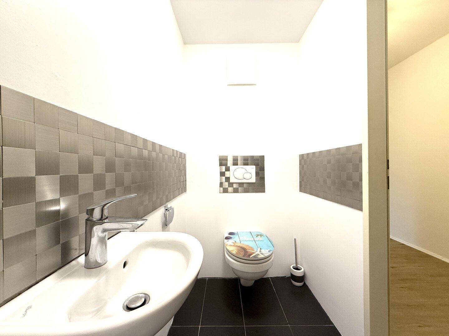 Kompaktes Gäste-WC mit modernem Design, kleinem Waschbecken und dunklen Bodenfliesen.