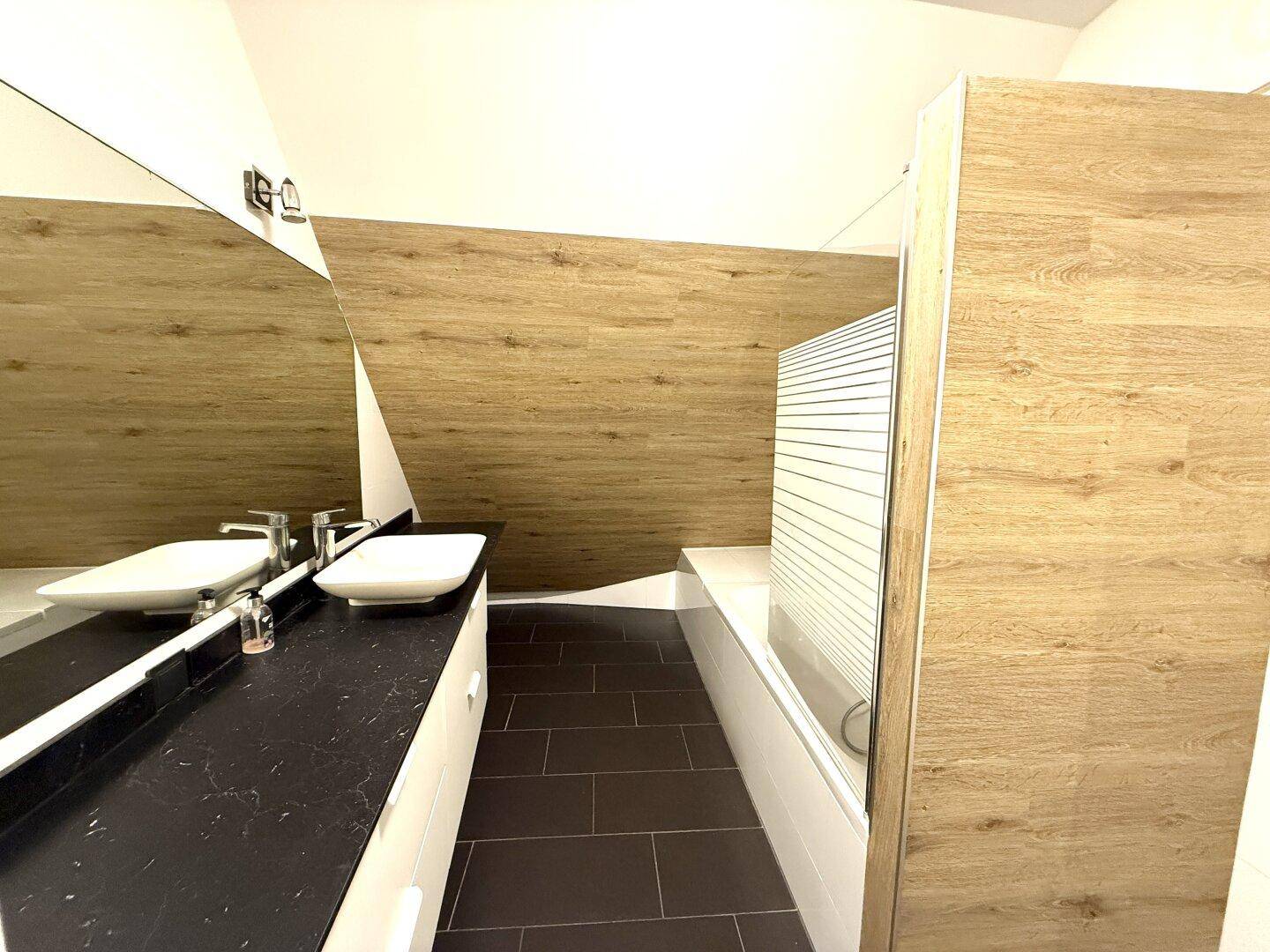 Modernes Badezimmer mit Doppelwaschbecken, dunkler Arbeitsplatte und Badewanne unter der Dachschräge.