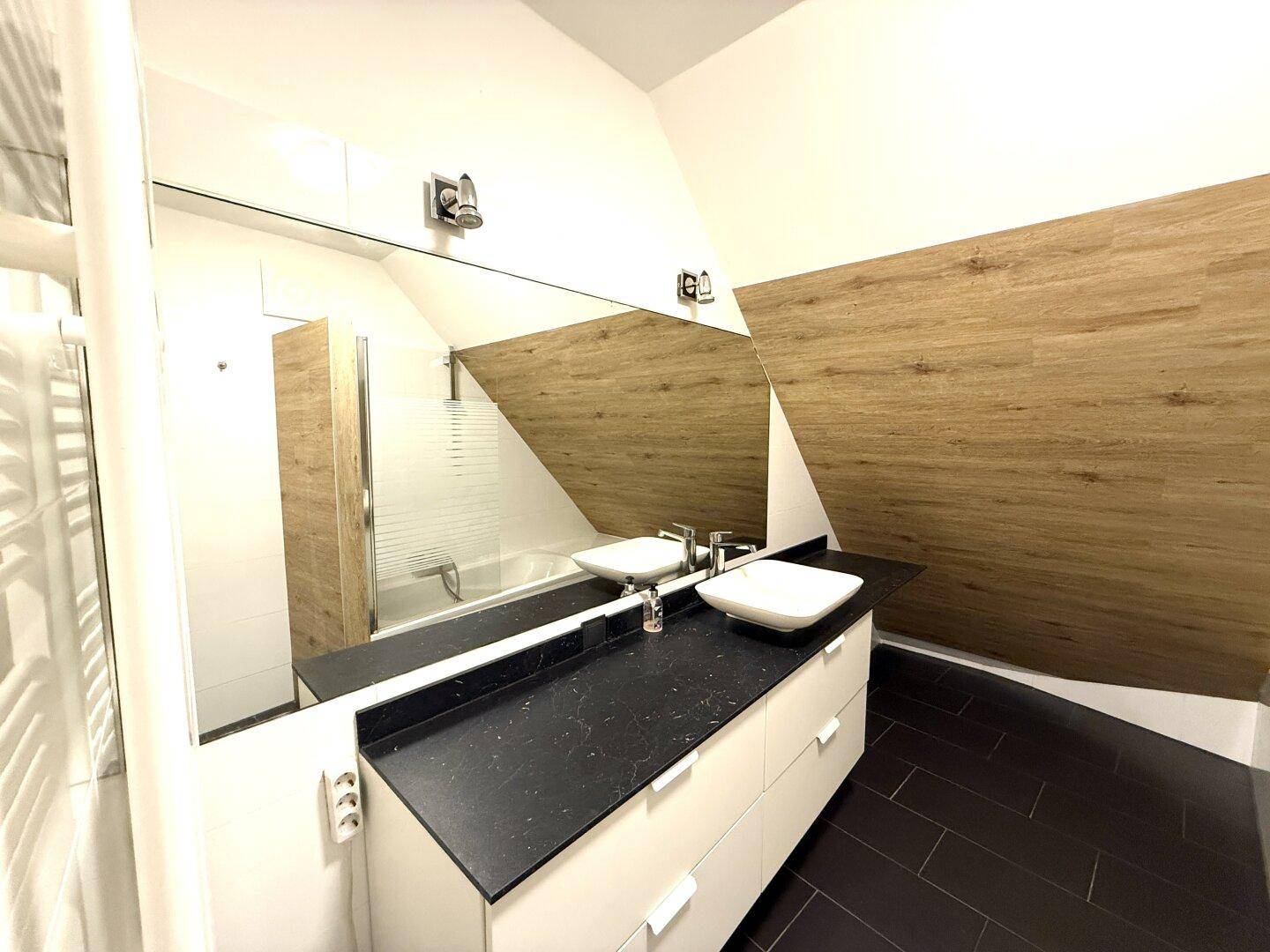 Helles Badezimmer mit Doppelwaschbecken, großem Spiegel und Badewanne unter der Dachschräge.