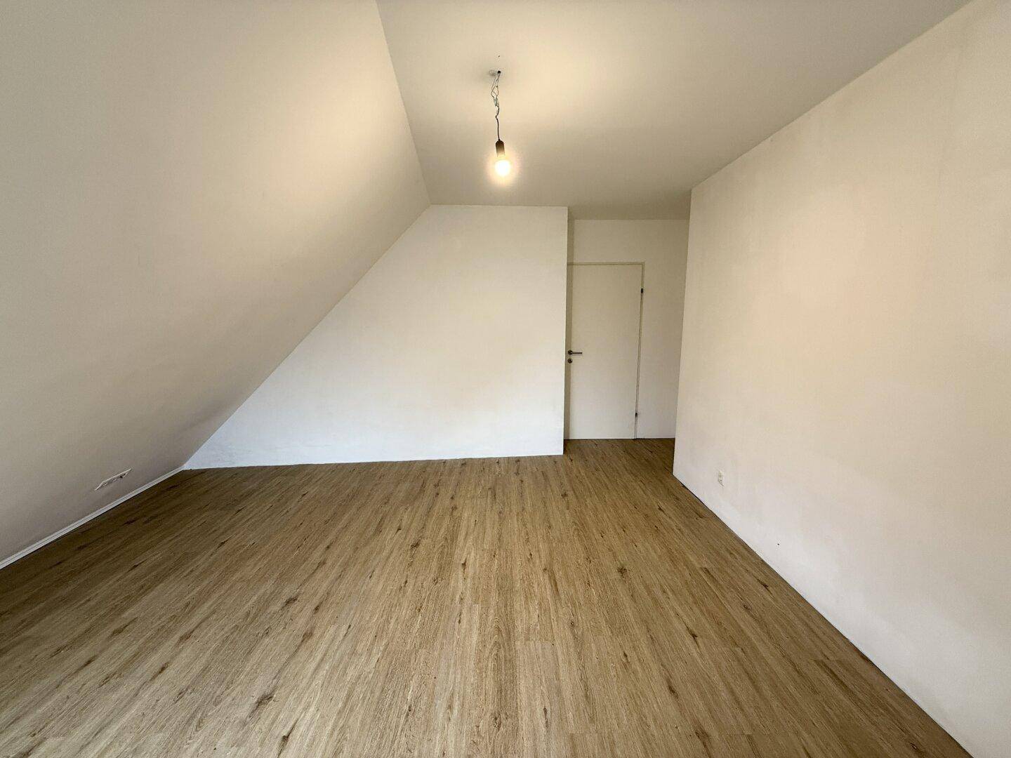 Helles Dachgeschosszimmer mit Laminatboden und weißer Tür, bietet eine gemütliche Atmosphäre.