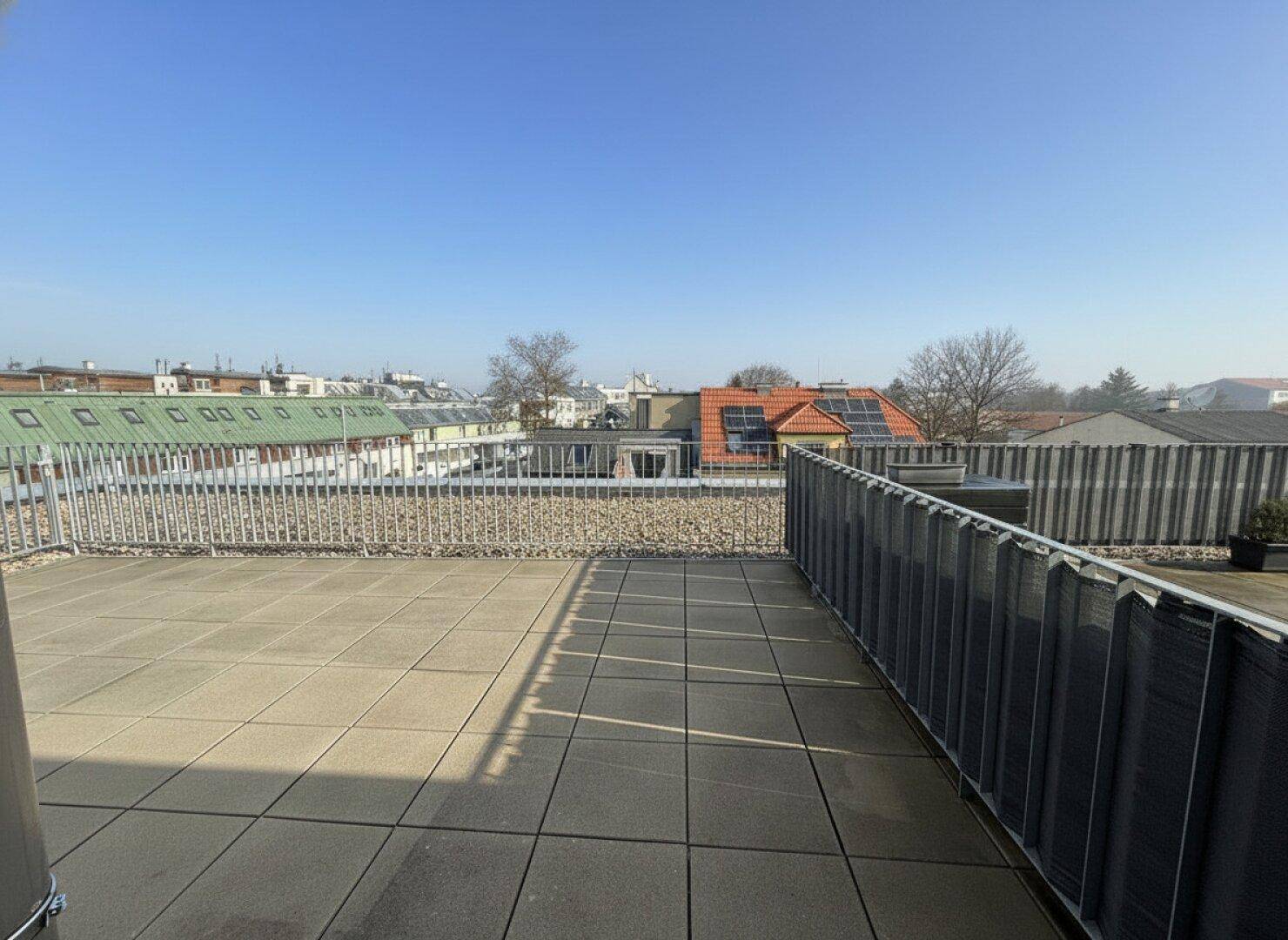 Geräumige Dachterrasse mit Fliesenboden und Metallgeländer, bietet einen weiten Blick über die Stadt.