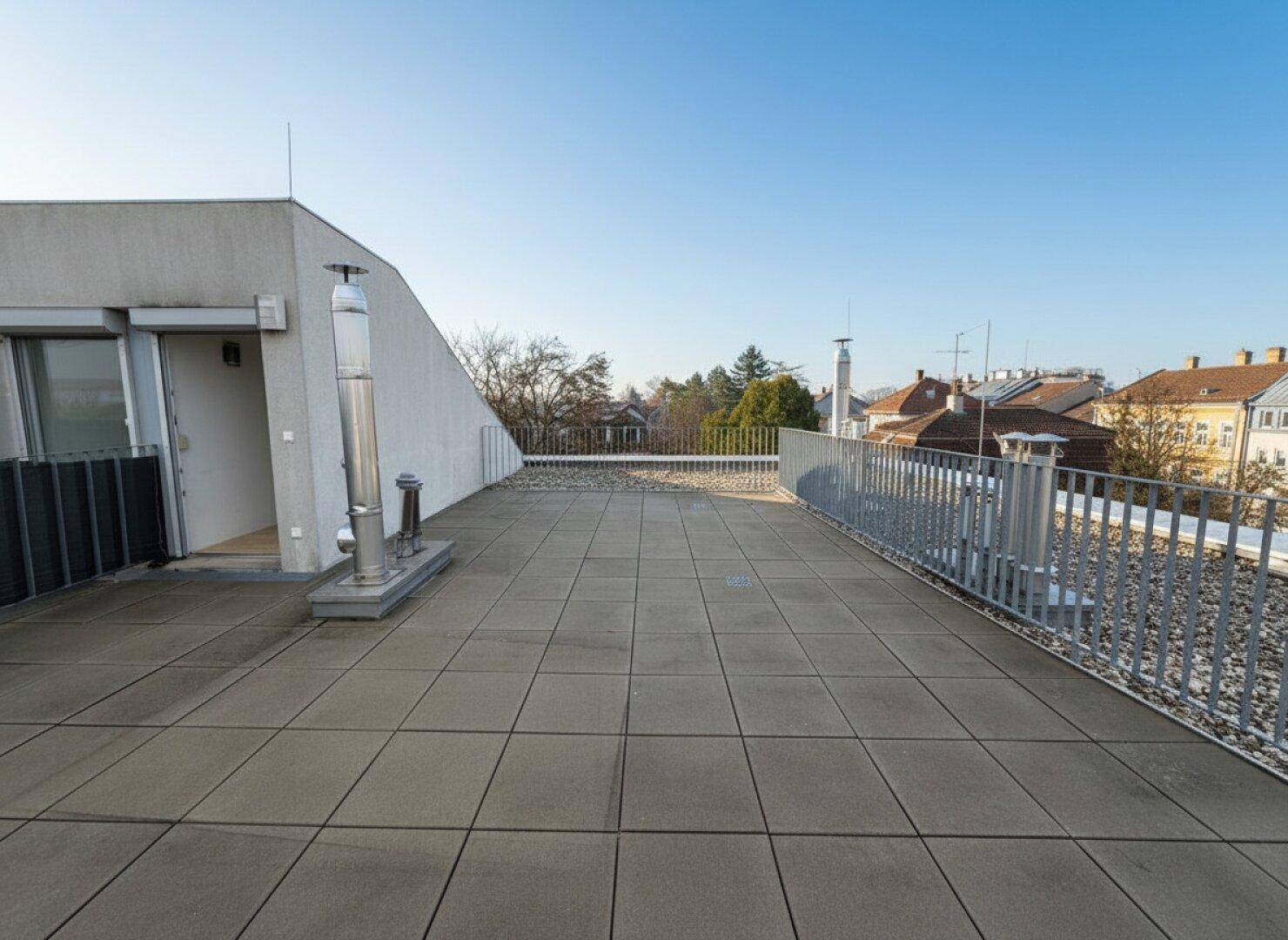 Große Dachterrasse mit Zugang zum Gebäude und Panoramablick auf die städtische Umgebung.