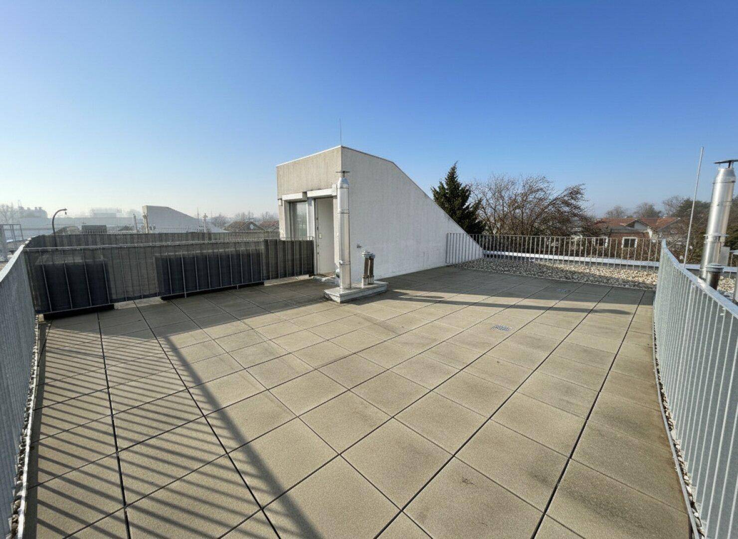Geräumige Dachterrasse mit Fliesenboden und weitem Blick über die Umgebung an einem sonnigen Tag.