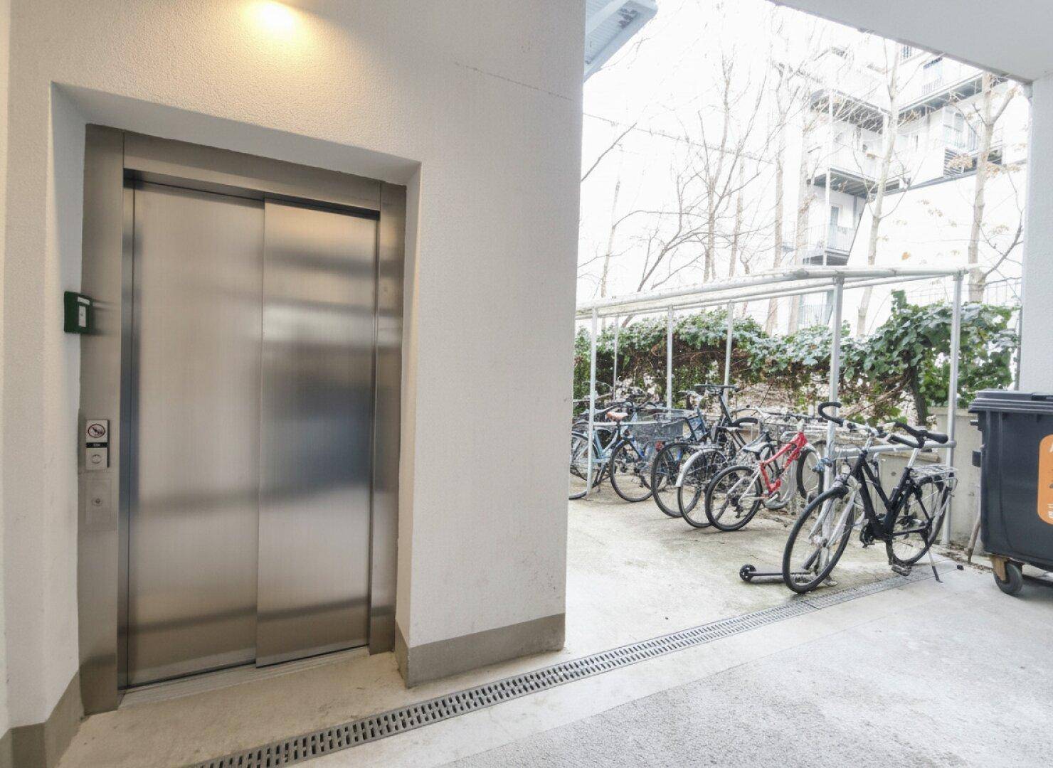 Moderner Aufzug im Eingangsbereich mit Fahrradabstellplatz im Freien.