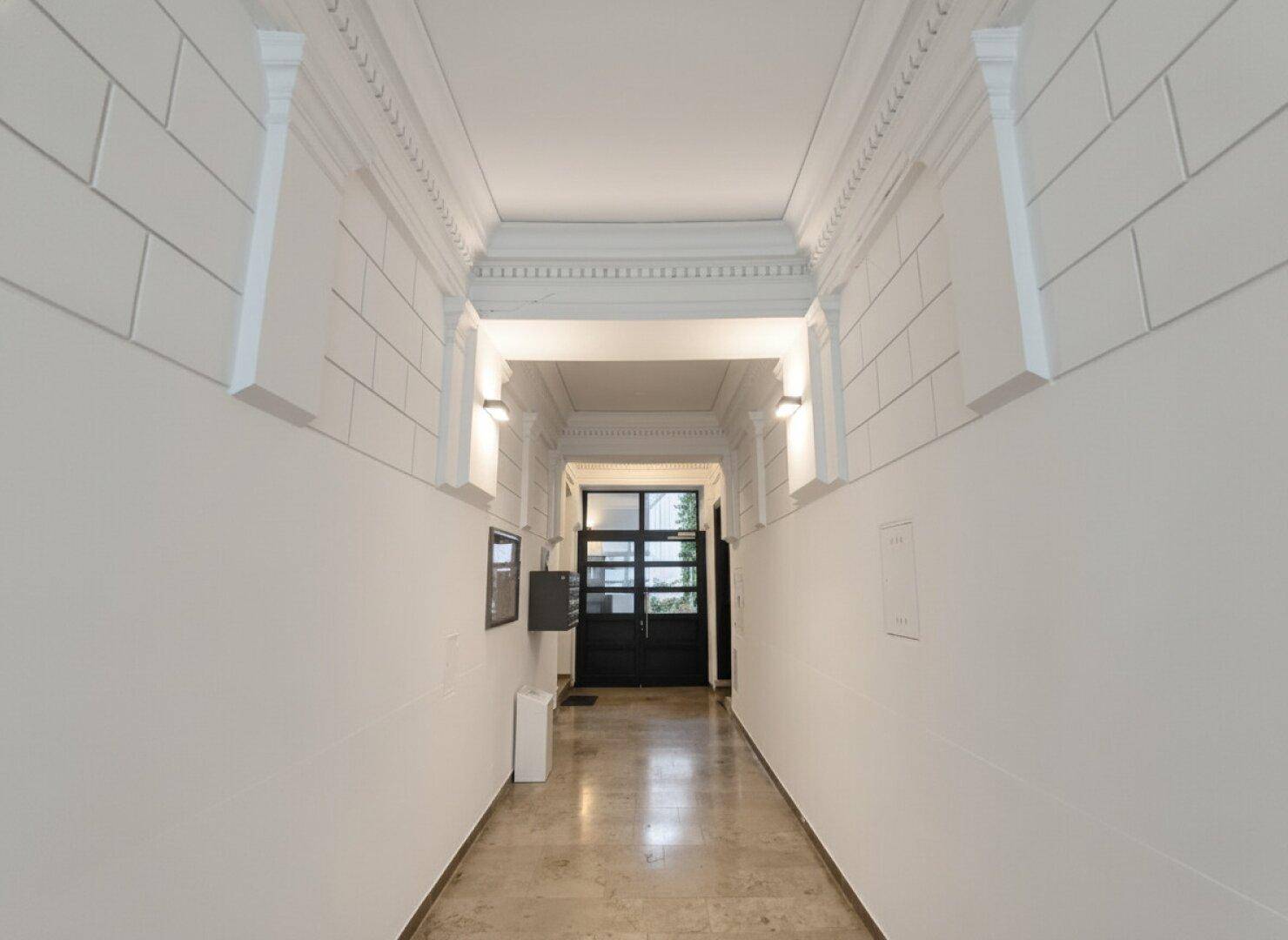 Eingangsbereich des Gebäudes mit Stuckdecke und klassischer Architektur.