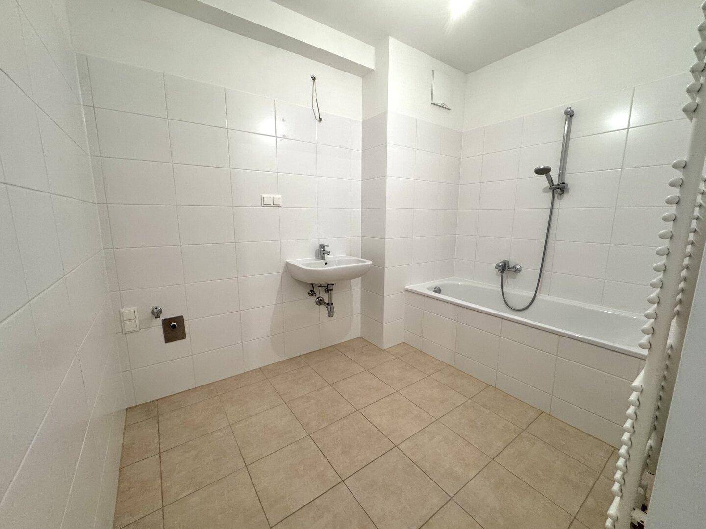 Funktionales Badezimmer mit Badewanne, Waschbecken und weißen Fliesen an Wänden und Boden.