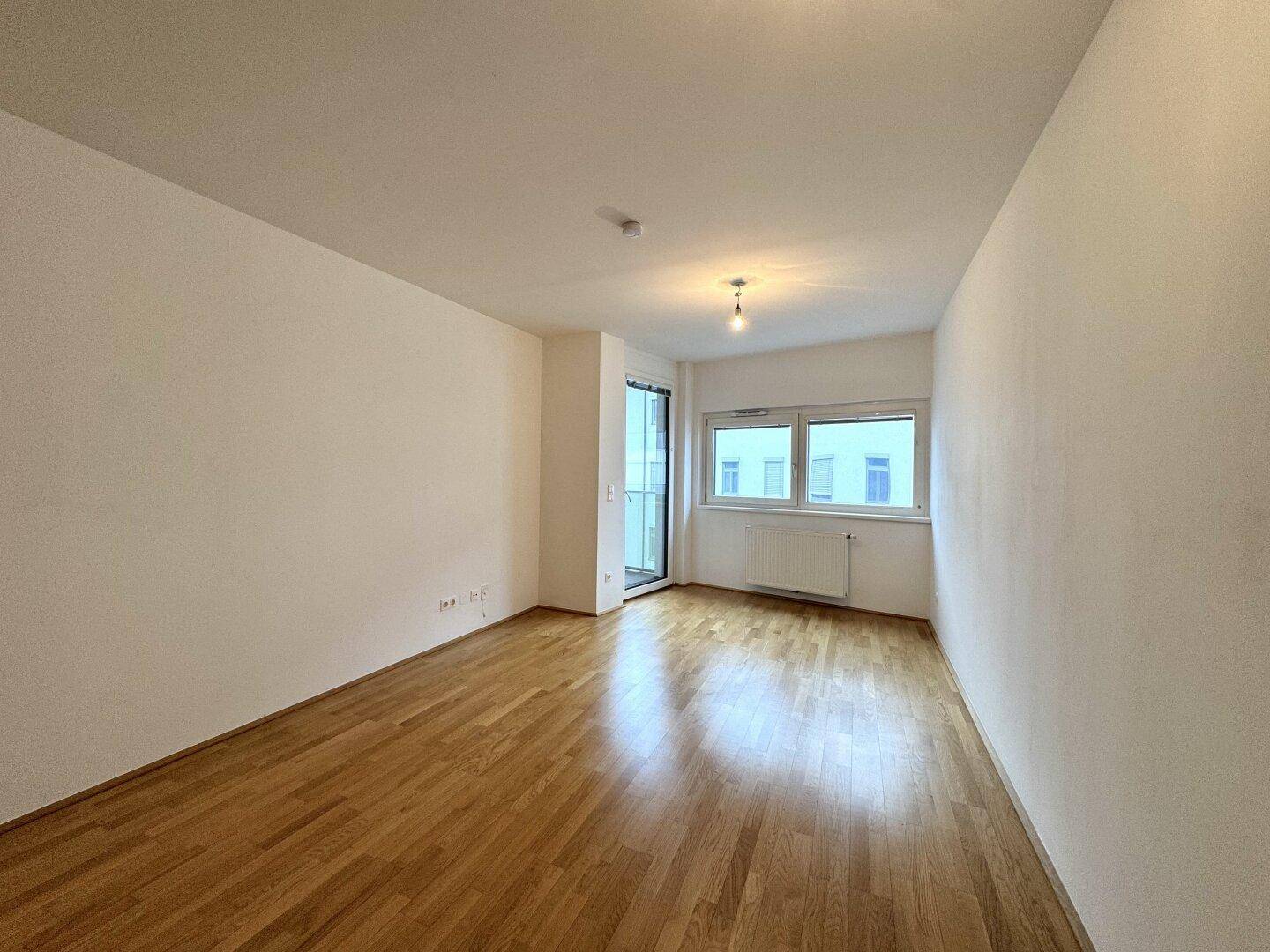 Helles Zimmer mit Parkettboden und Zugang zu einem Balkon, ideal als Wohn- oder Schlafzimmer.