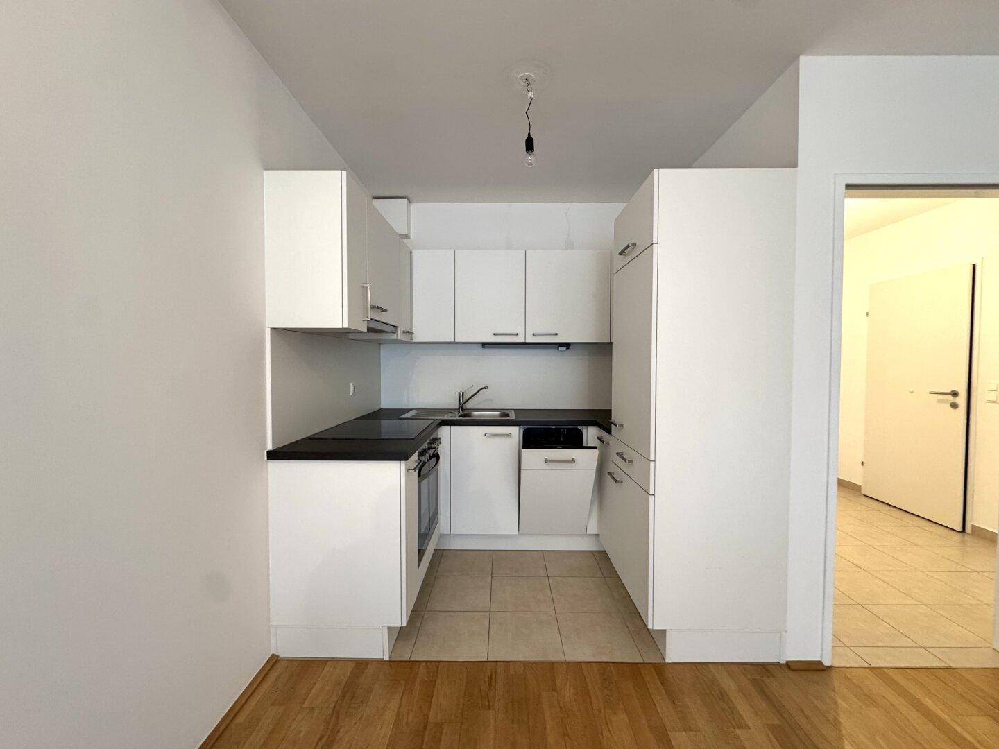 Moderne Einbauküche mit weißen Schränken, dunkler Arbeitsplatte und Fliesenboden.