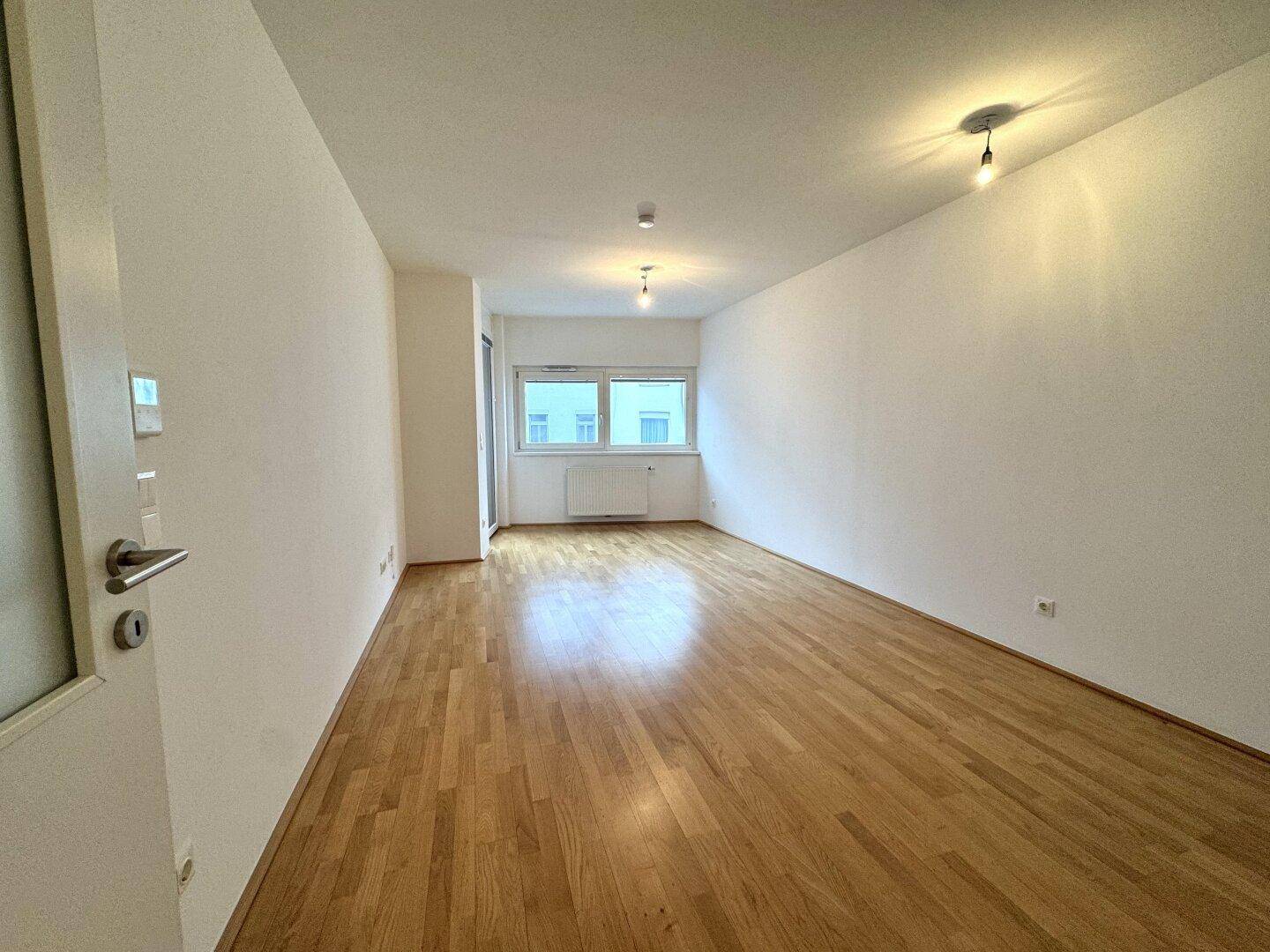 Geräumiges Zimmer mit hellem Parkettboden und großen Fenstern, vielseitig nutzbar.