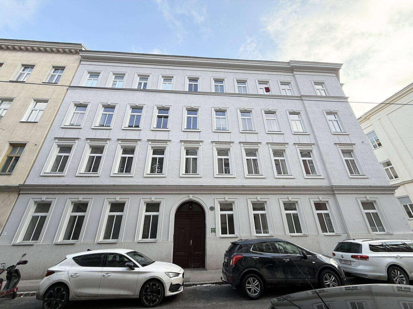 Klassische Fassade eines Mehrfamilienhauses mit vielen Fenstern und parkenden Autos.
