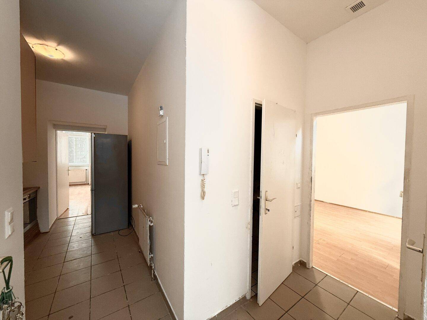 Flur mit Fliesenboden, Gegensprechanlage und Blick in die Küche und weitere Zimmer.