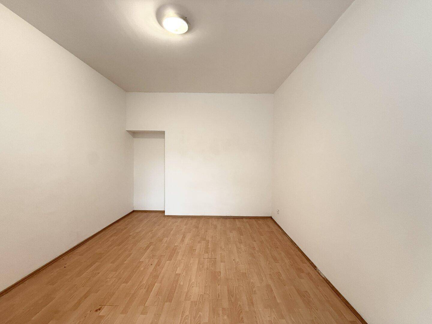 Leerer Raum mit Laminatboden und einem Türrahmen, der auf weitere Zimmer führt.
