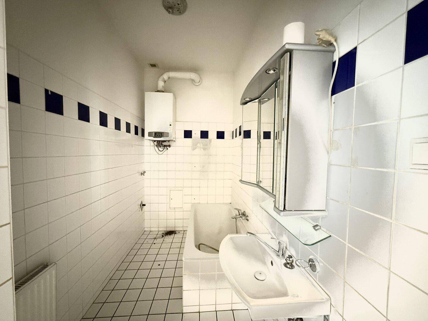 Gefliestes Badezimmer mit Waschbecken, Badewanne und Gastherme, in gutem Zustand.