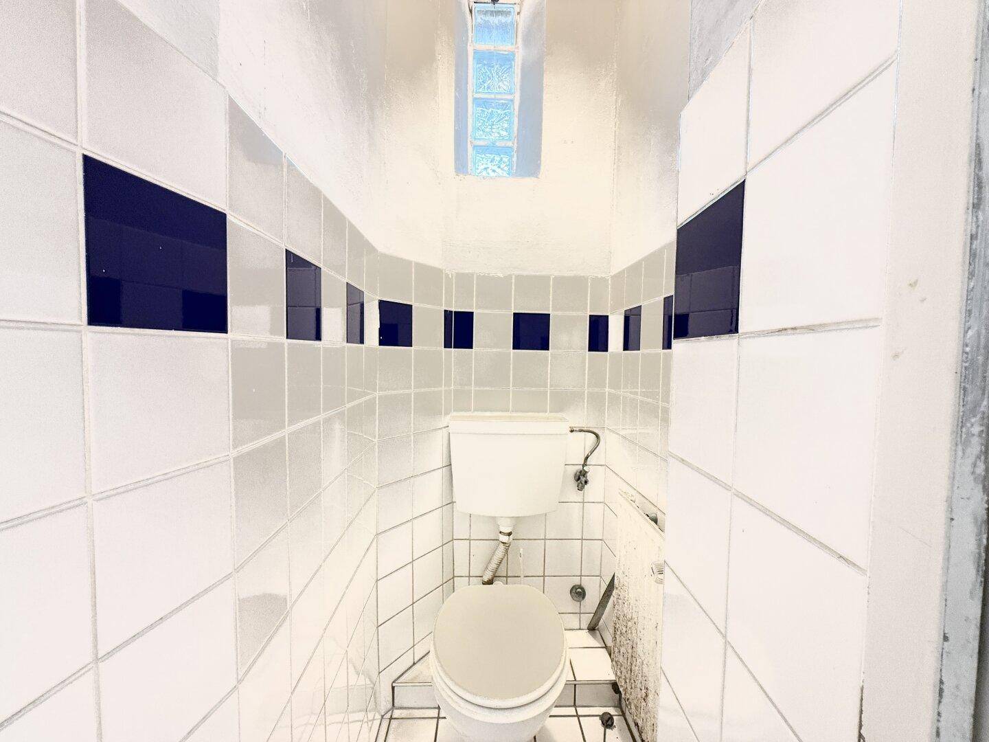 Kleines WC mit Fliesen an Wänden und Boden, ausgestattet mit einer Toilette.