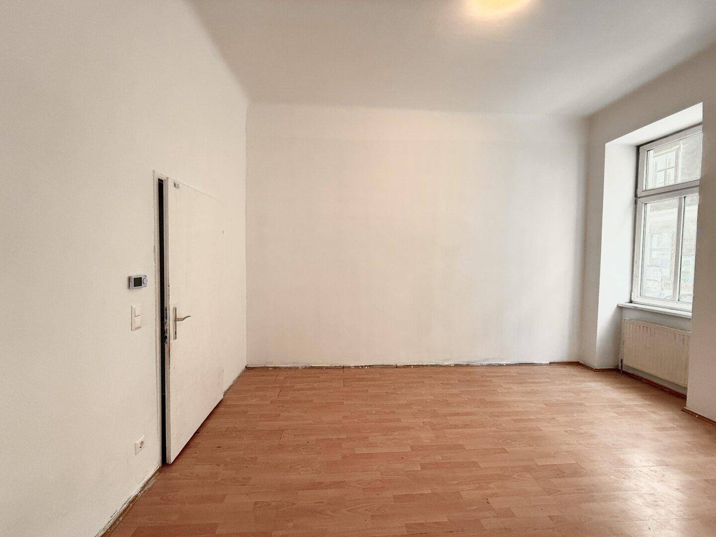 Geräumiges, leeres Zimmer mit Laminatboden und einem Fenster, ideal für Wohnzwecke.