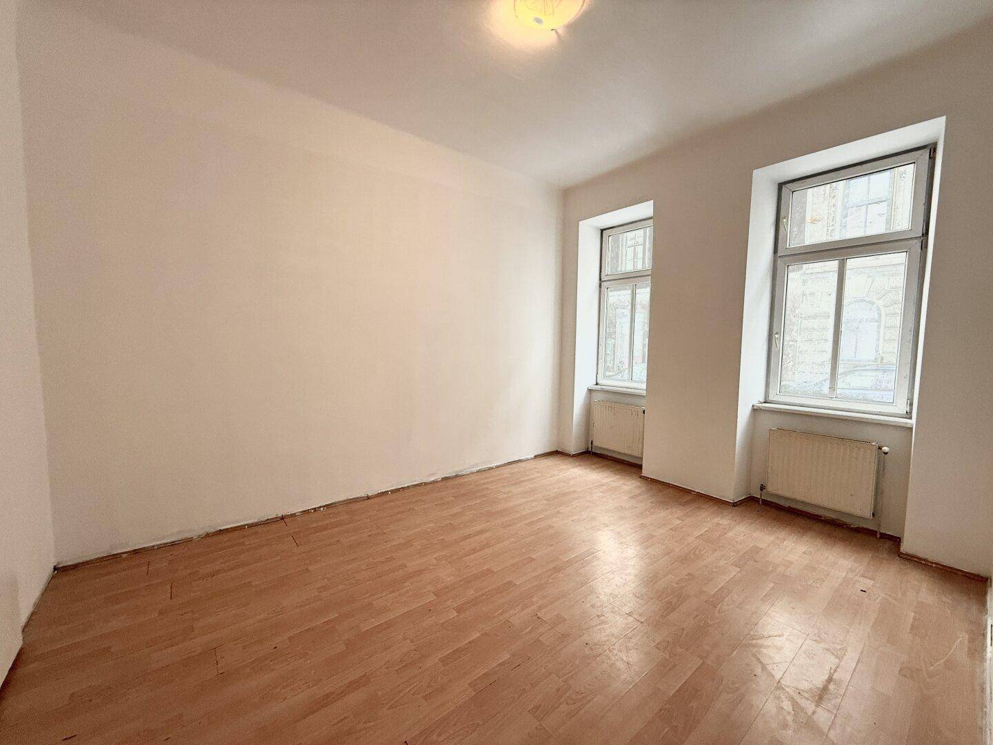 Helles, leeres Zimmer mit Laminatboden und zwei Fenstern, bietet viel Gestaltungspotenzial.