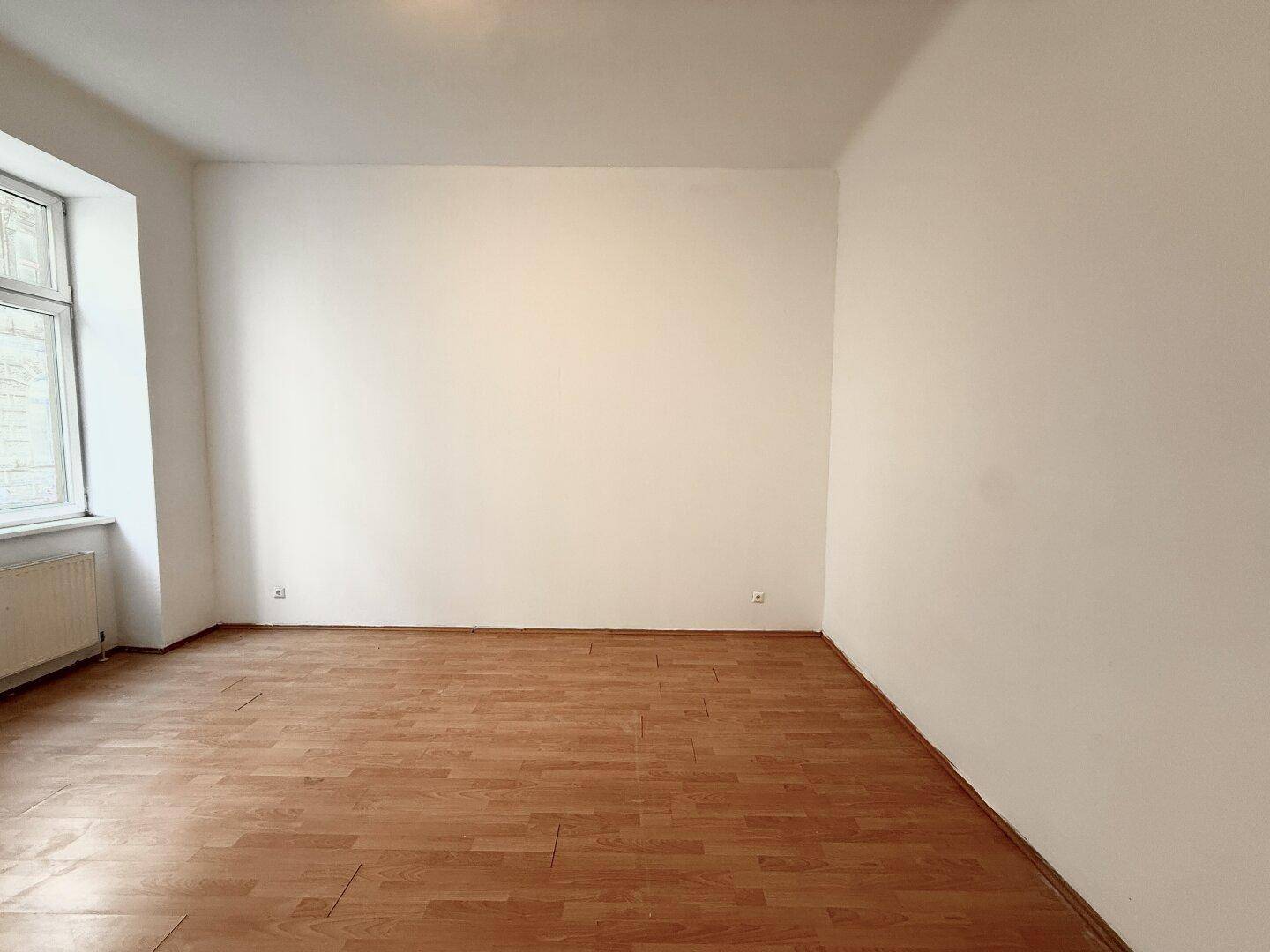 Geräumiges, leeres Zimmer mit Laminatboden und einem Fenster, ideal für verschiedene Nutzungen.
