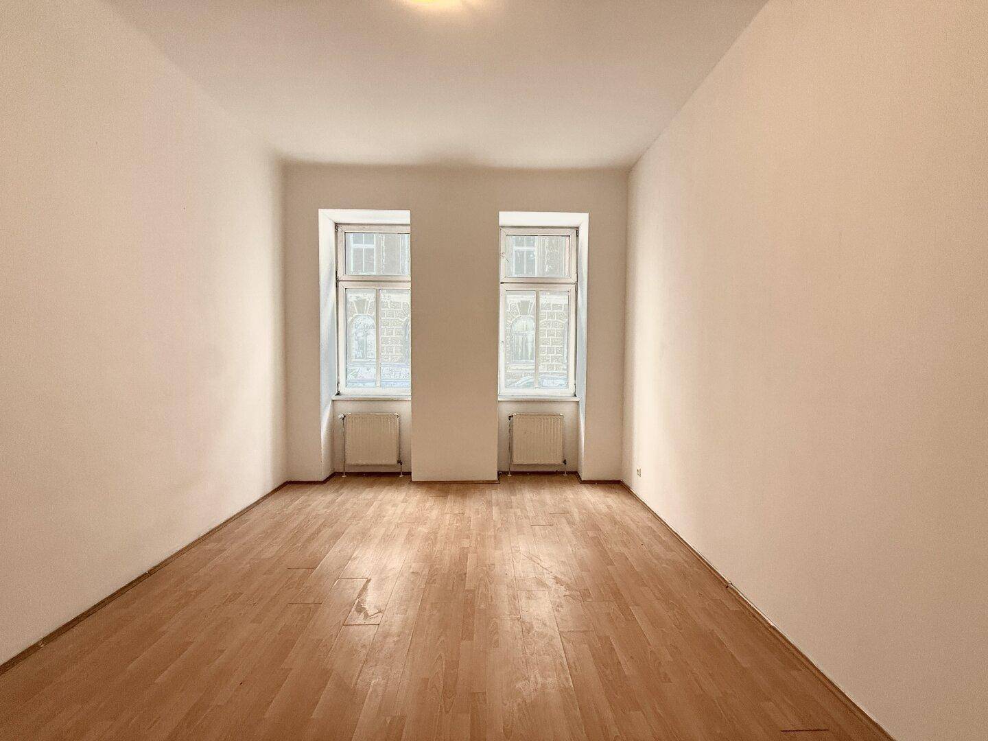 Helles, leeres Zimmer mit Laminatboden und zwei Fenstern, bereit für neue Bewohner.