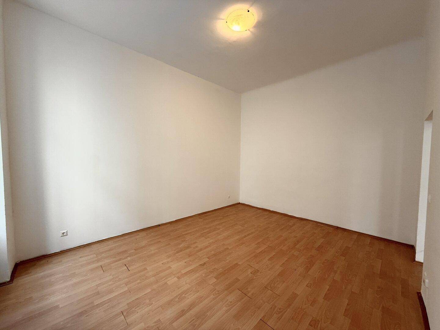 Leerer Raum mit Laminatboden und einer Ecke, die auf weitere Gestaltungsmöglichkeiten wartet.
