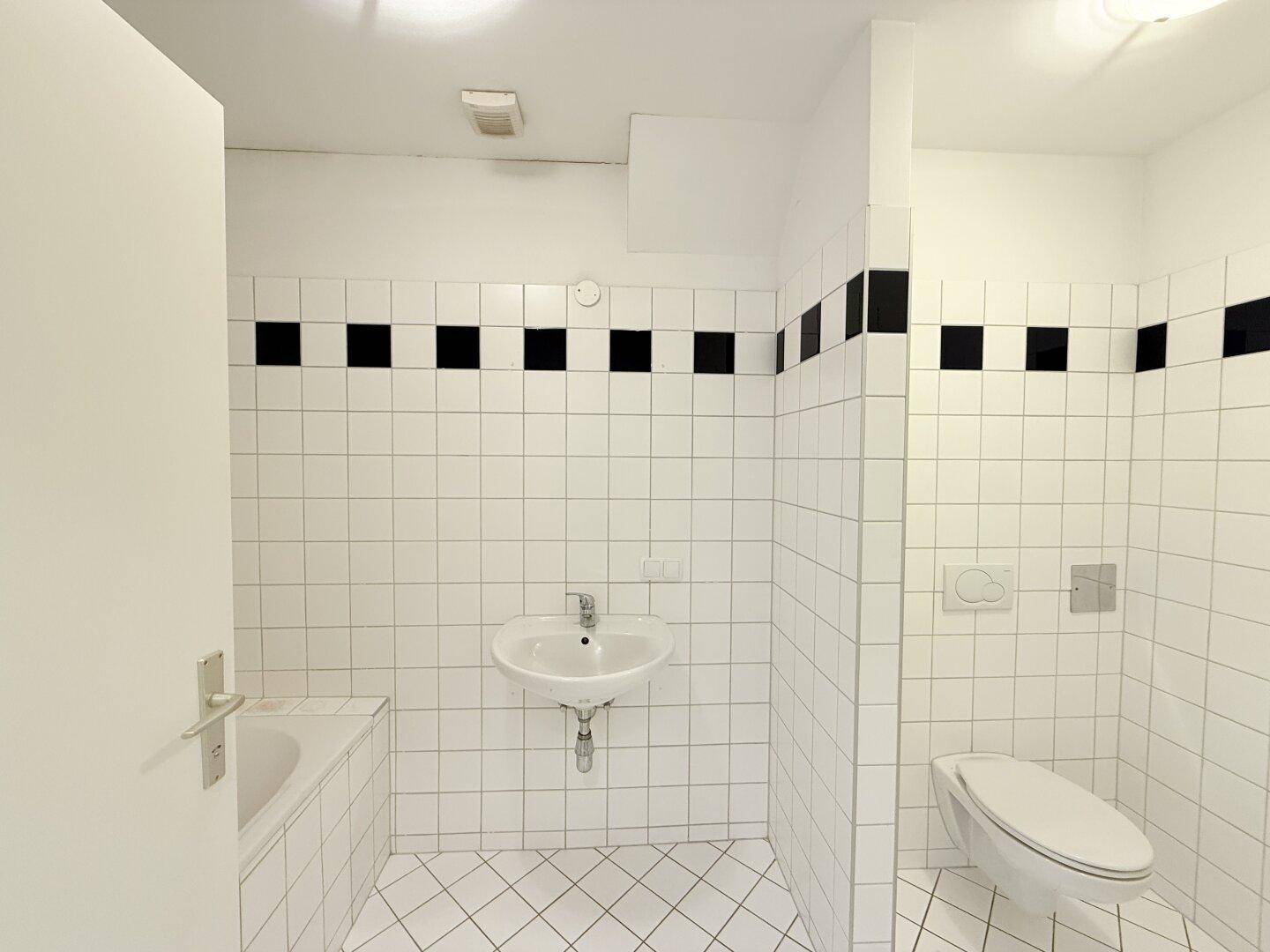 Gefliestes Badezimmer mit Badewanne, Waschbecken und WC, akzentuiert durch schwarze Fliesen.