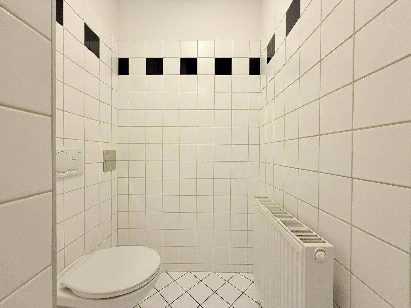 Separates WC mit weißen Fliesen, Wand-WC und Heizkörper, in sauberem Zustand.