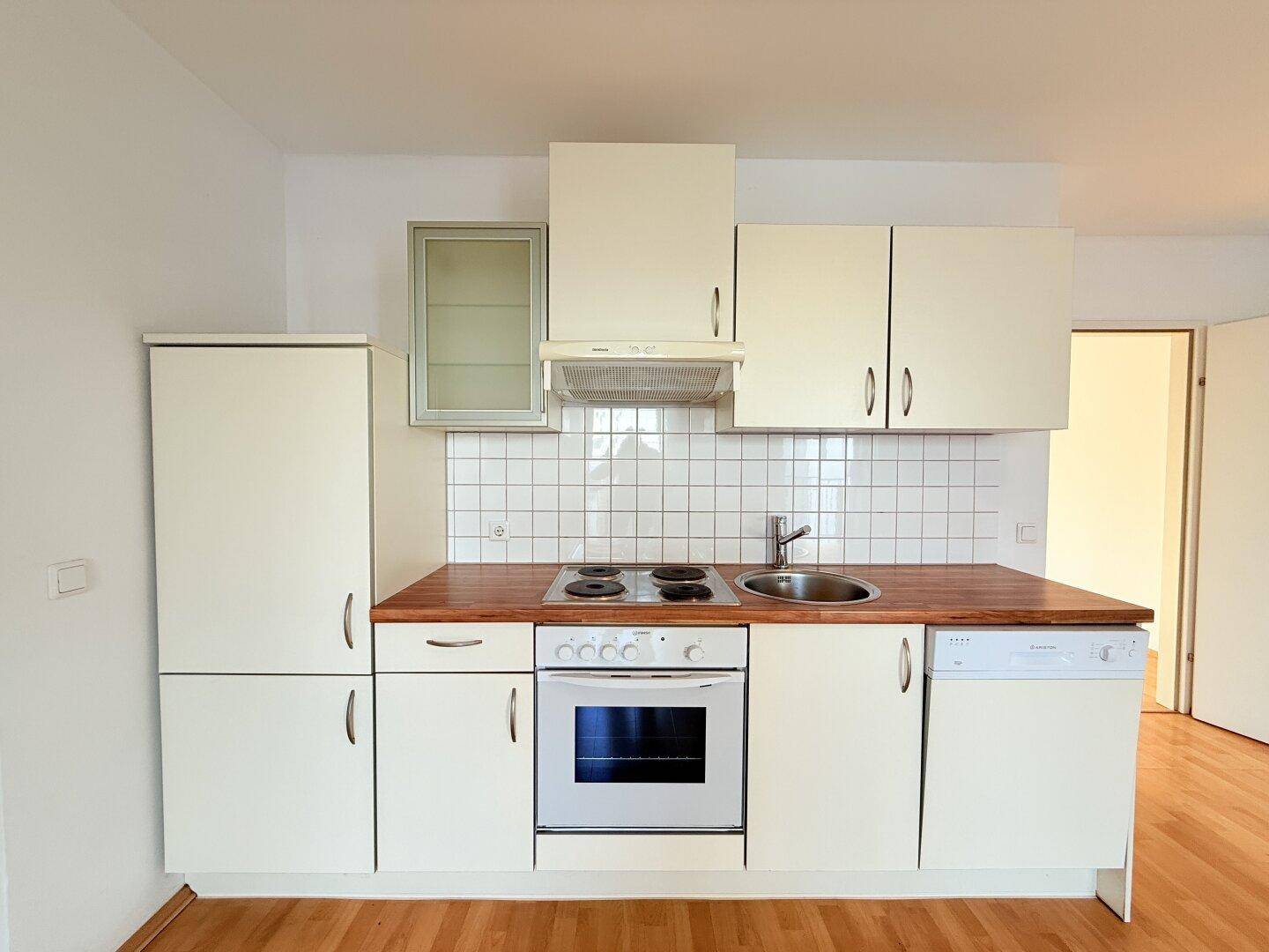 Kompakte Küchenzeile mit weißen Schränken, Holz-Arbeitsplatte und grundlegenden Einbaugeräten.