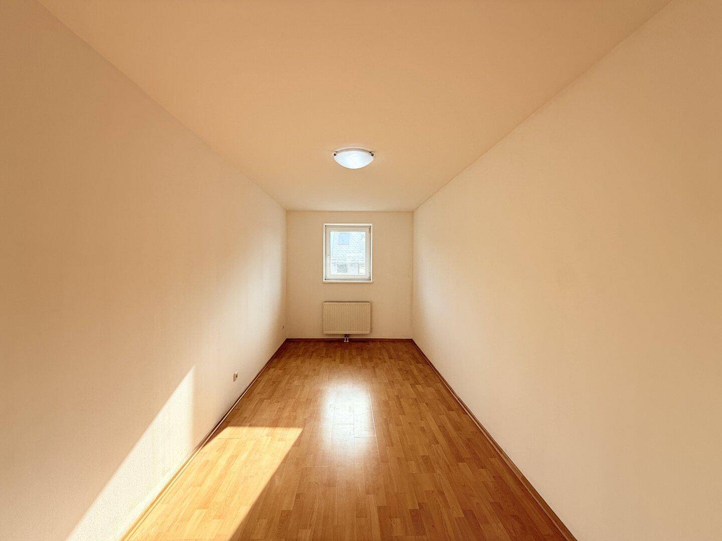 Schmaler Raum mit Parkettboden und einem Fenster, das natürliches Licht hereinlässt.