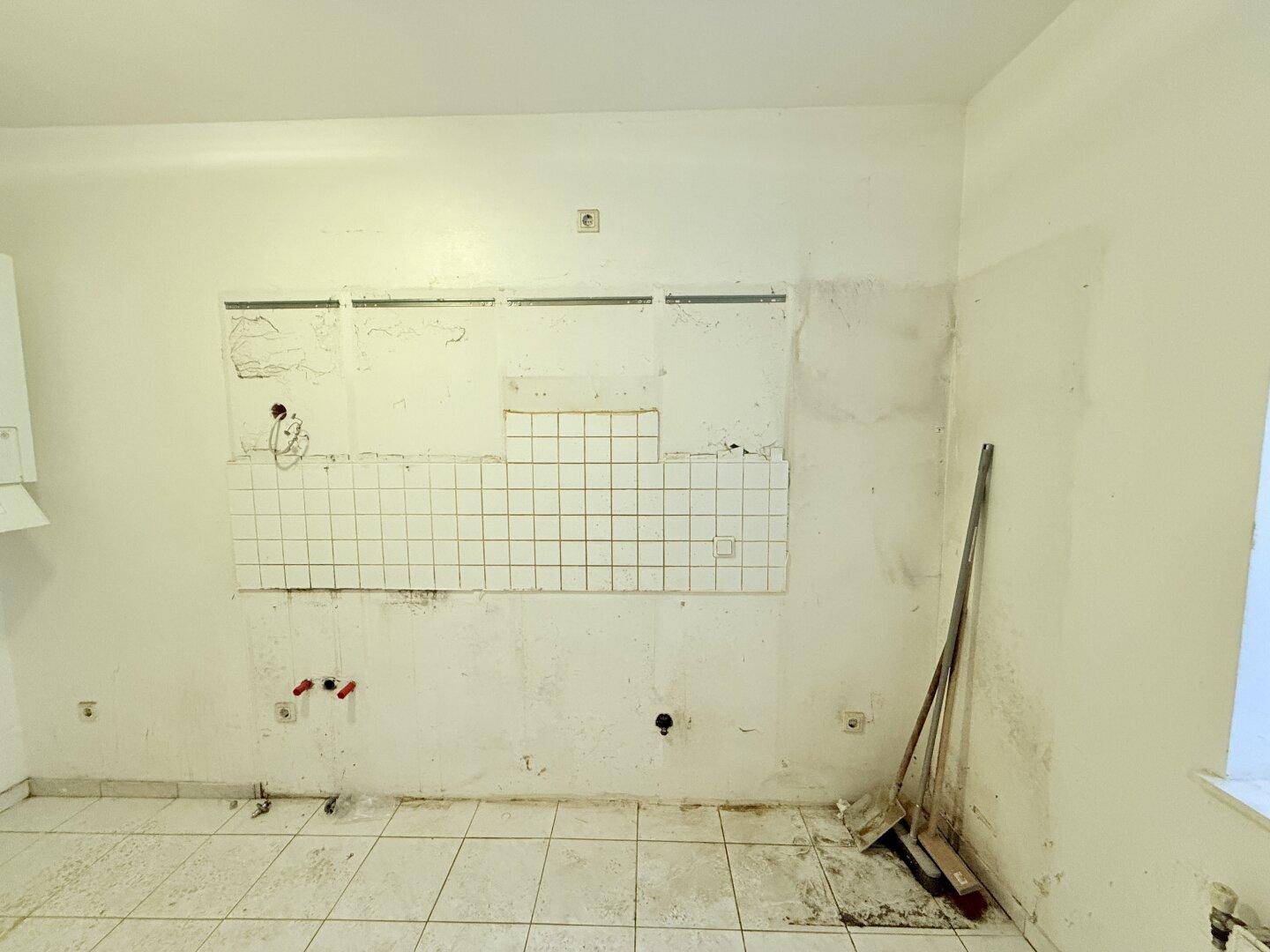 Detailansicht der Küchenwand mit alten Fliesen und Anschlüssen, bereit für eine Modernisierung.