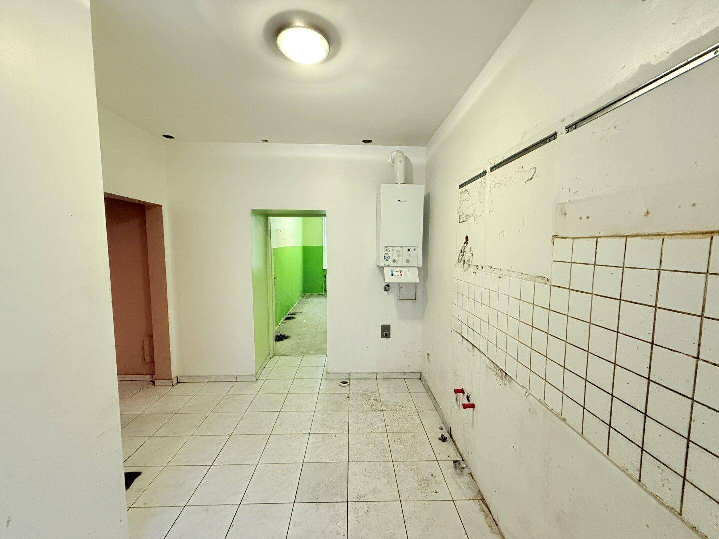 Leere Küche mit Fliesenboden, Gastherme und vorbereiteten Anschlüssen für eine neue Küchenzeile.