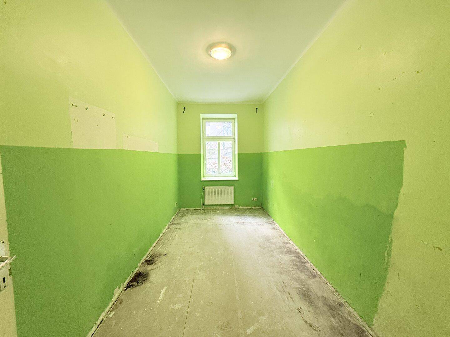 Kleines Zimmer mit auffälligen grünen Wänden, Fenster und Heizkörper, ideal für eine individuelle Gestaltung.