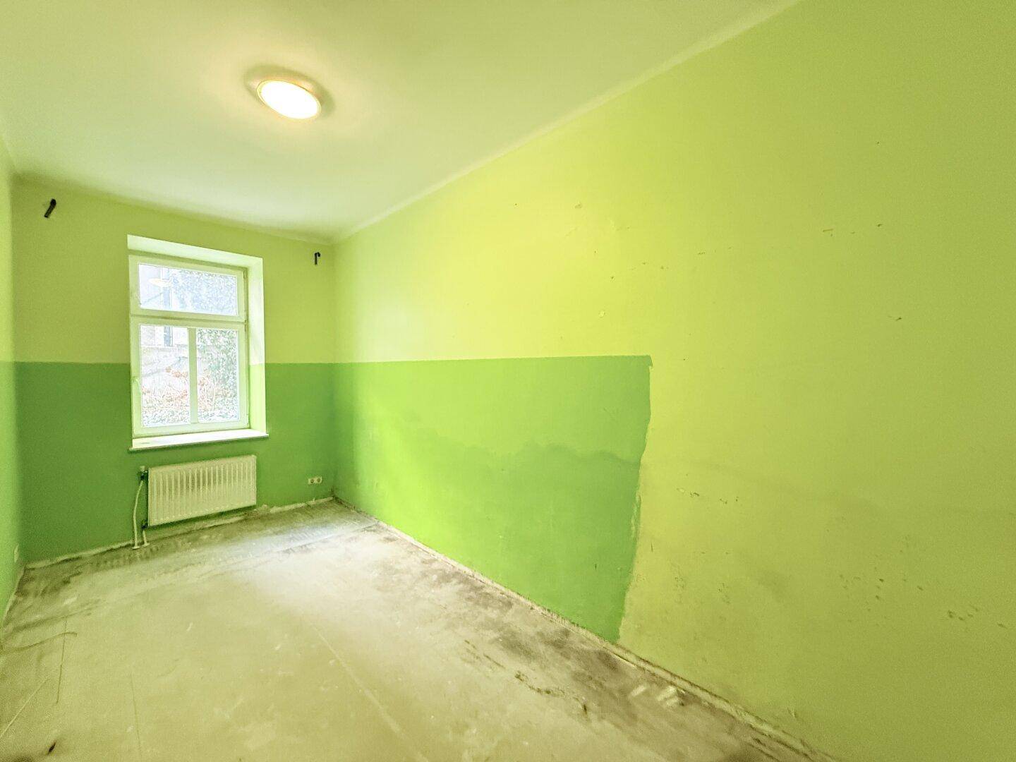 Helles Zimmer mit grünen Wänden und Fenster, bietet Potenzial für eine moderne Renovierung.