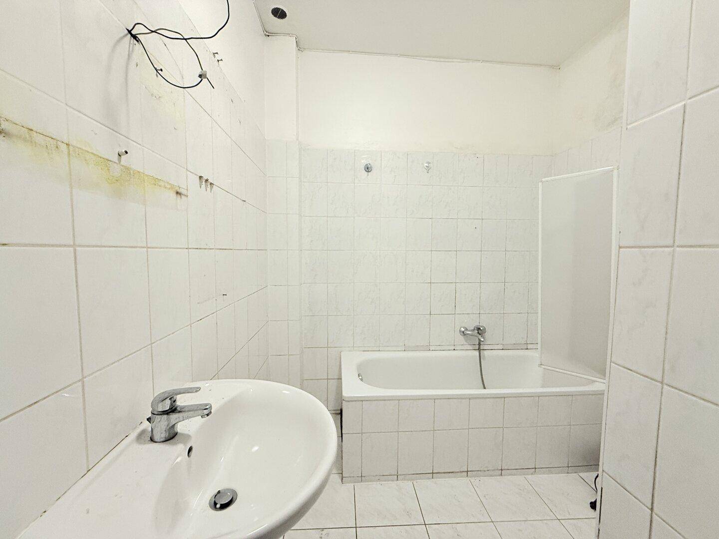 Badezimmer mit Badewanne, Waschbecken und weißen Fliesen, benötigt eine umfassende Renovierung.