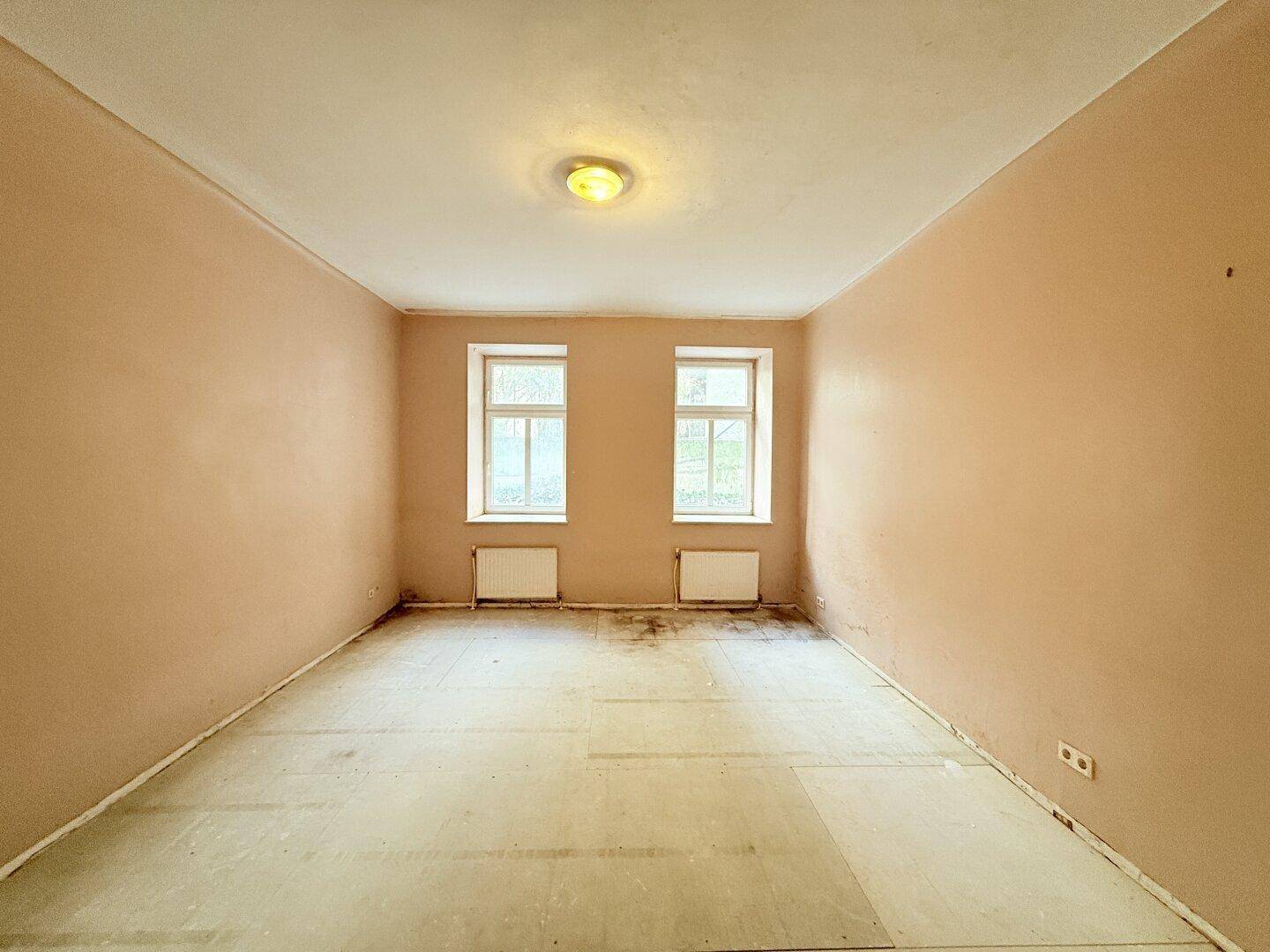 Geräumiges Zimmer mit zwei Fenstern und beigefarbenen Wänden, bietet viel Gestaltungspotenzial.
