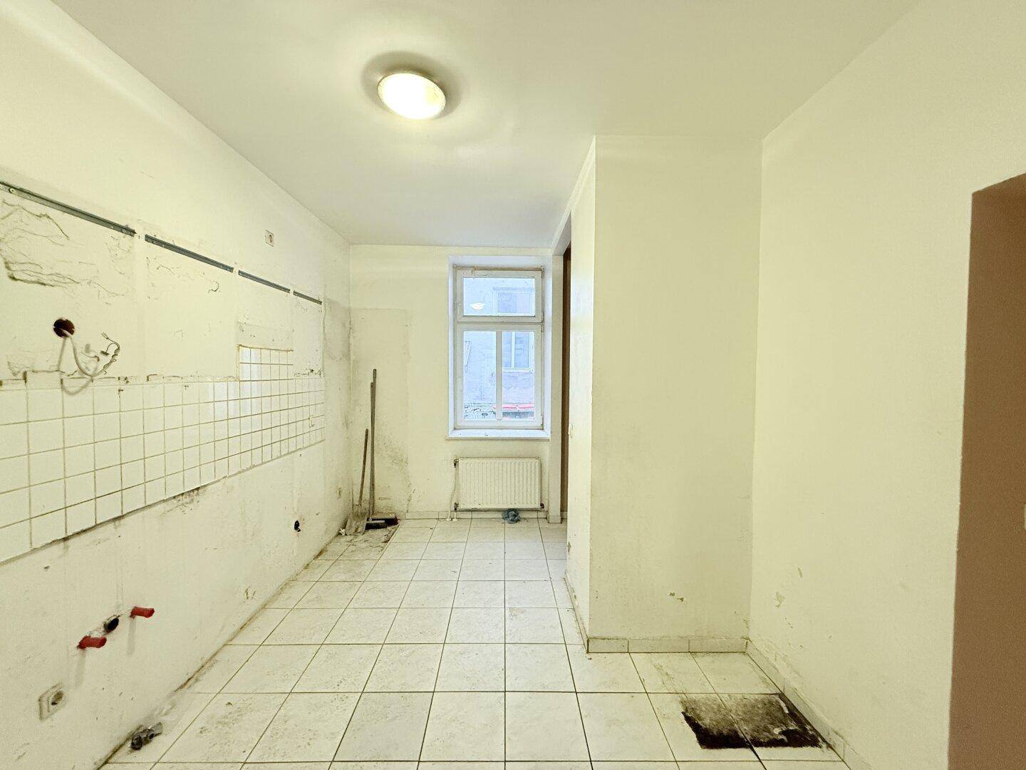 Küche mit Fliesenboden, Fenster und Heizkörper, bereit für die Installation einer neuen Küchenzeile.